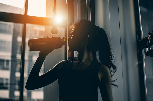 A woman sticks to her daily creatine and hydration habit by drinking her electrolyte mix from a shaker bottle right after her workout.