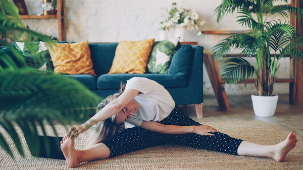 A woman practices a calming evening stretching routine at home, part of the sleep and recovery habits that pair well with steady hydration and electrolyte intake.