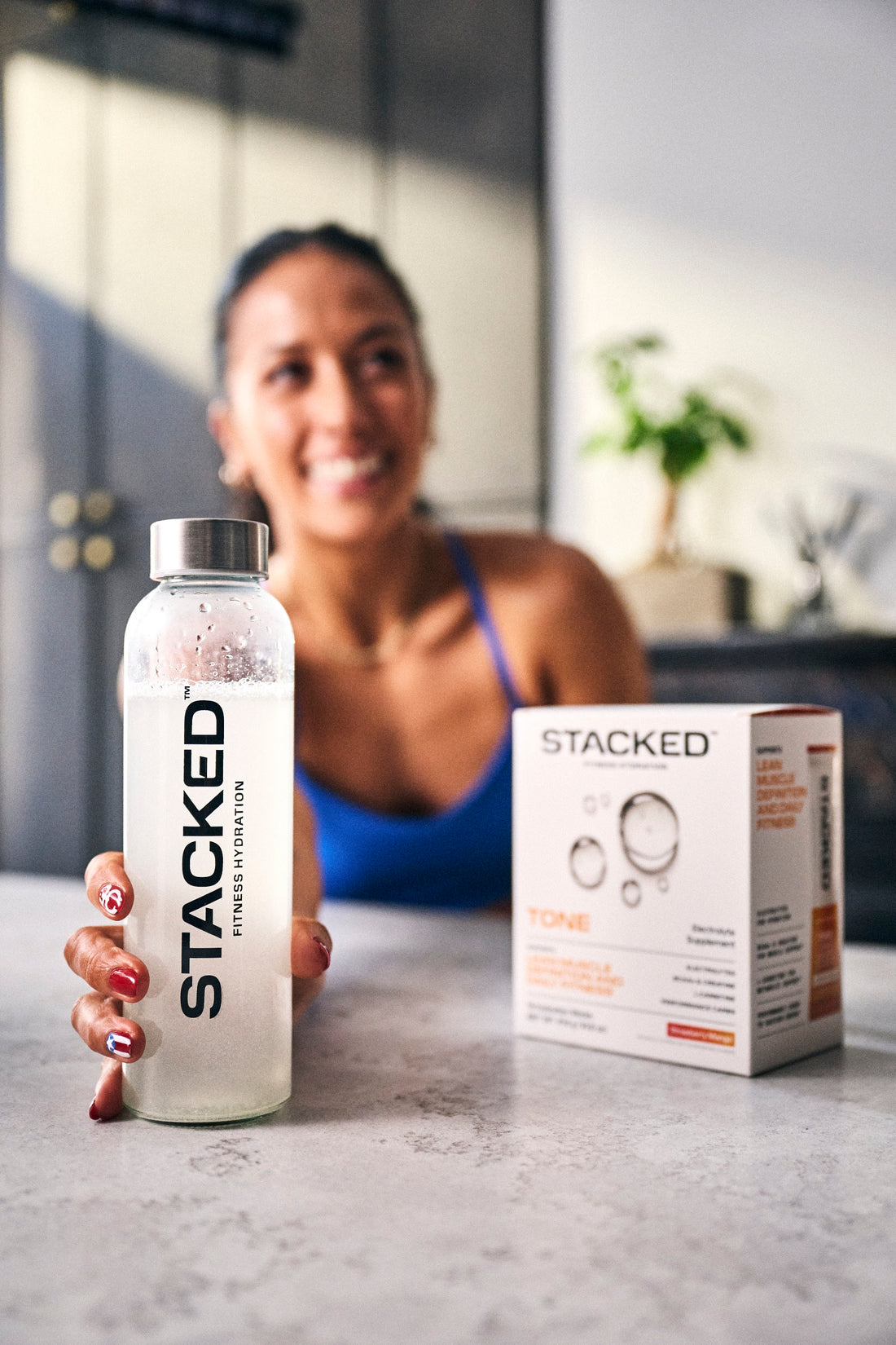 Smiling woman in her kitchen with a Stacked water bottle and a box of TONE