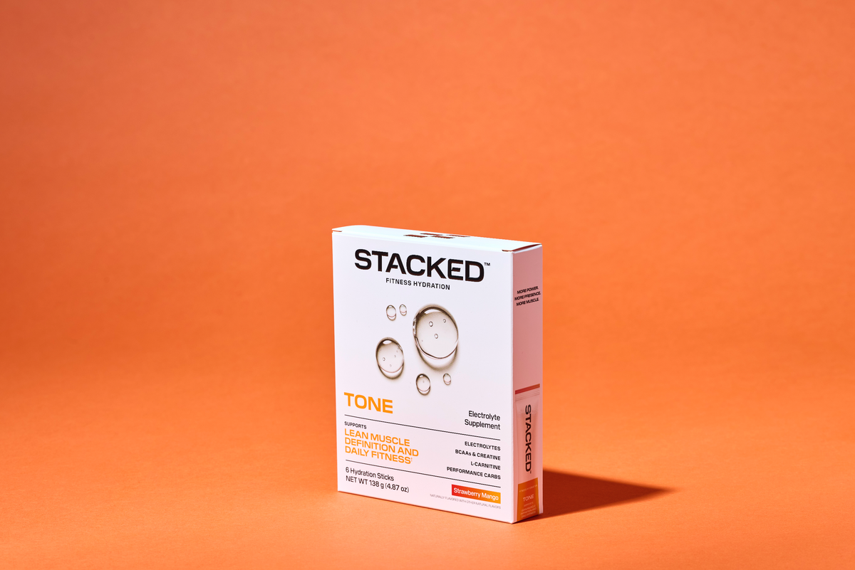A container of Stacked Fitness Hydration's TONE creatine and electrolyte hydration mix against an orange background, representing how electrolytes support creatine absorption for active adults.