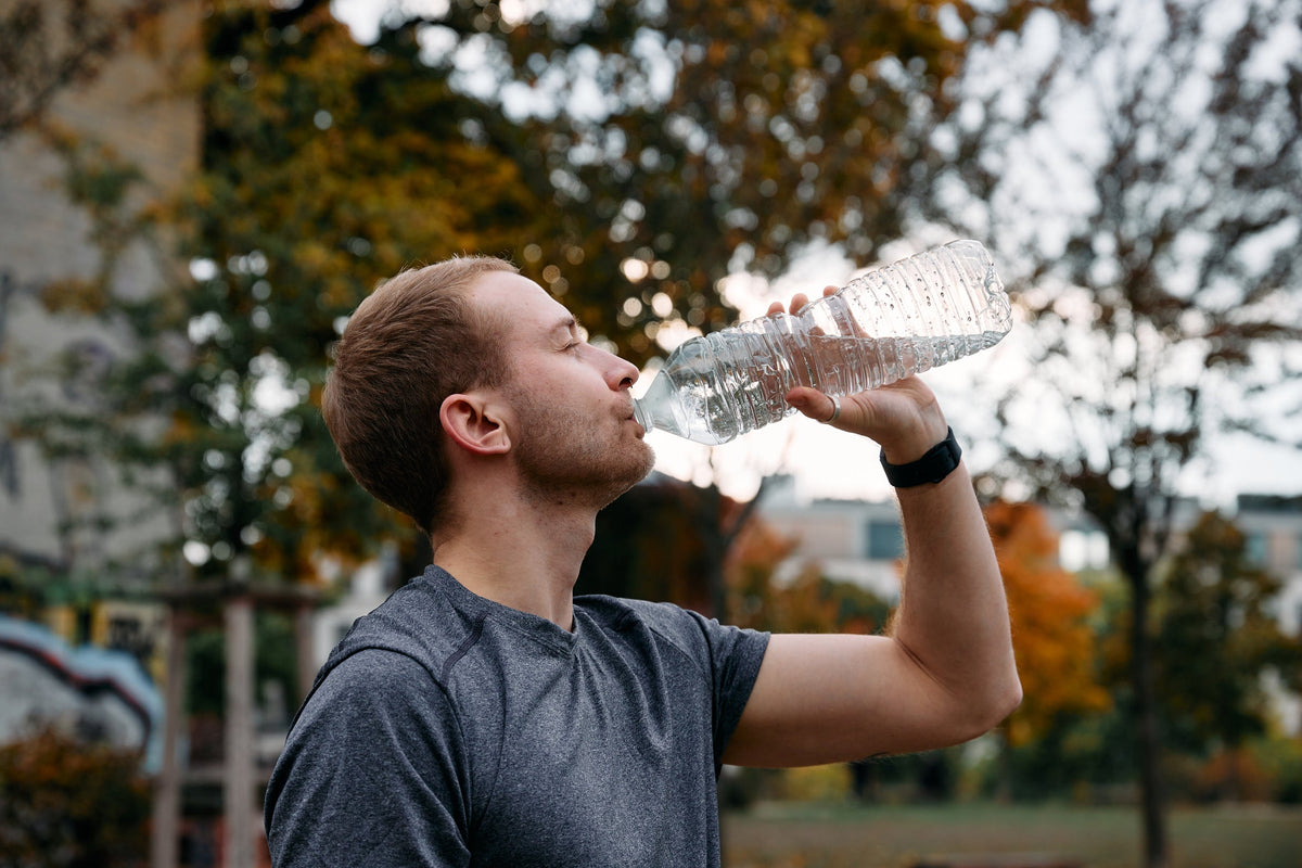 A man drinks from a water bottle in the park after training, rehydrating in the window where creatine and electrolytes absorption relies on sodium.