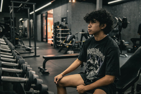 A young man sits on a gym bench, pausing before his workout as he considers whether creatine for beginners is worth trying before he's even started training.