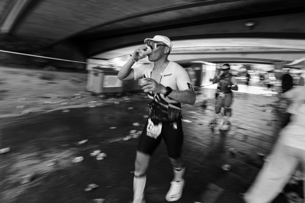 An endurance runner drinks water from a cup mid-race, a reminder that electrolyte deficiency symptoms can build up during intense exercise before they're noticed.
