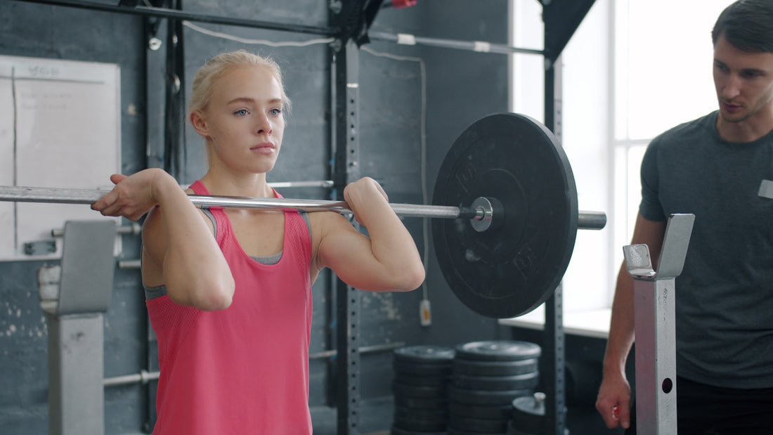 A woman focused mid-set during a barbell squat in the gym, the kind of demanding training session where dehydration and fluid loss can quietly undercut focus.