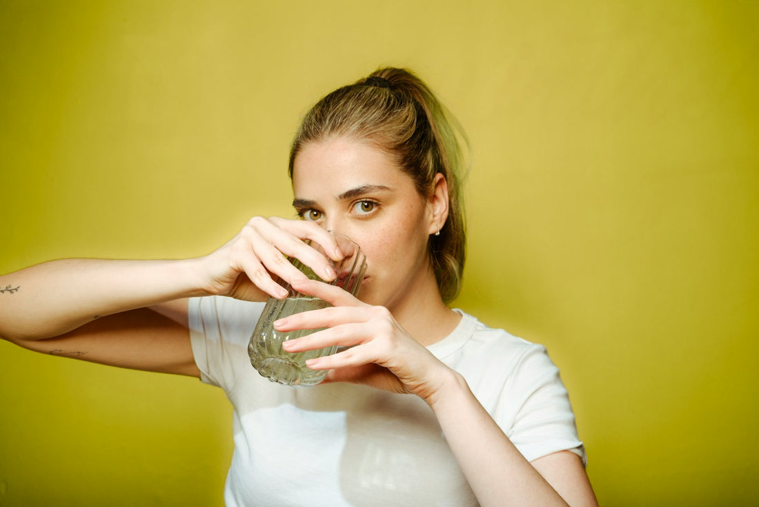 A woman drinks a full glass of water, illustrating the everyday hydration habit that supports skin health for active adults.