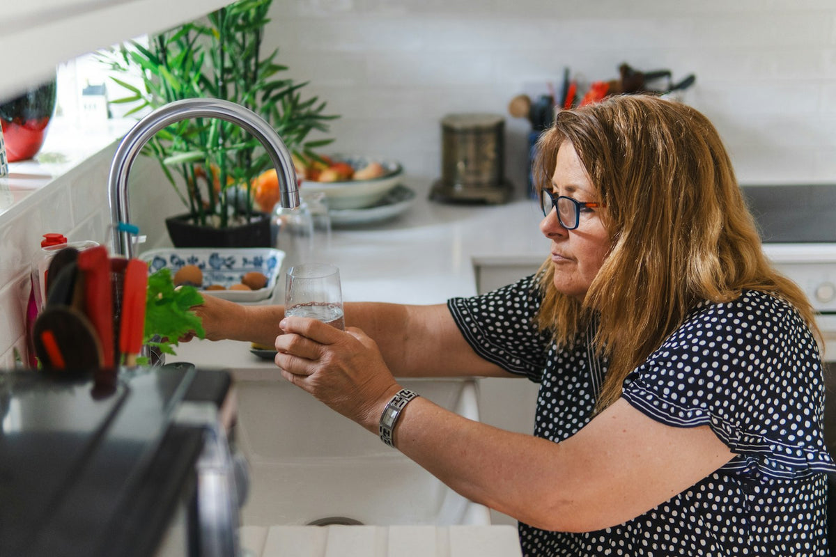 A woman filling a glass with water at her kitchen sink as part of a simple daily hydration habit