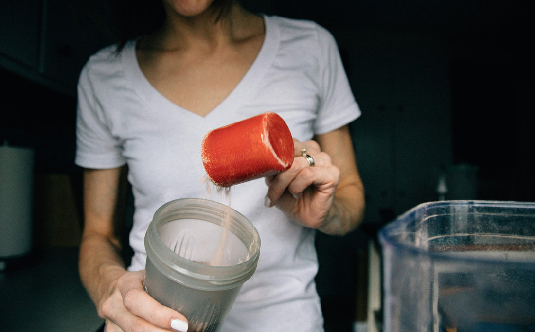 A woman pouring supplement powder into a glass to build her stacked water routine.