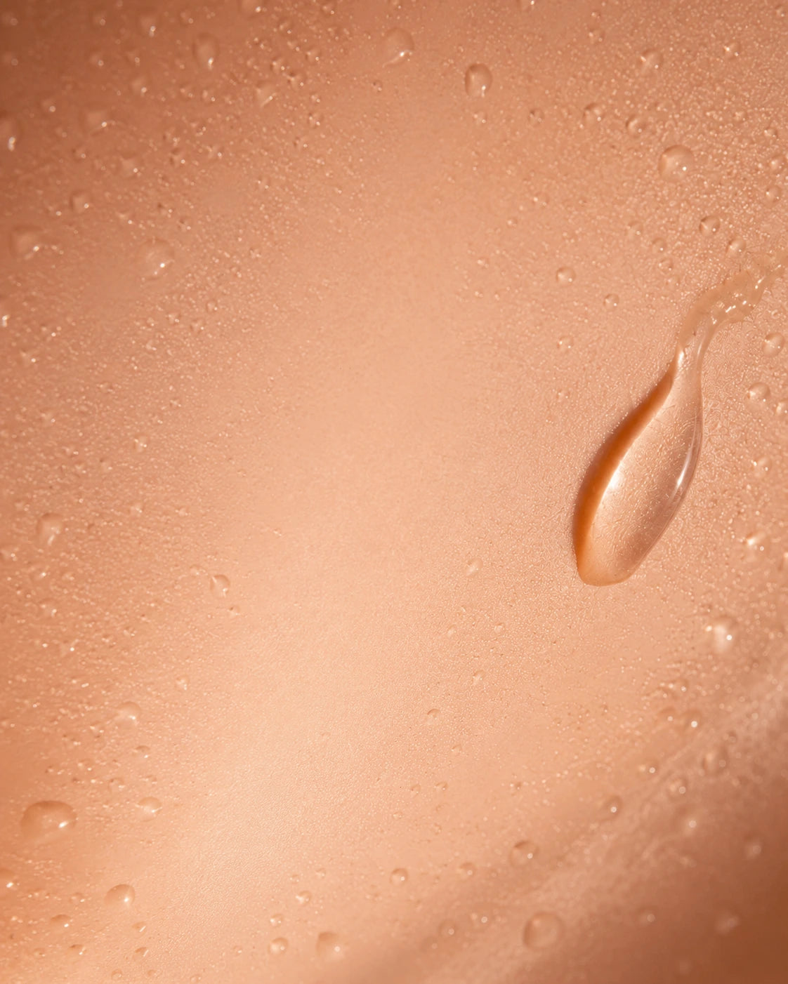 Close-up of a smooth peach-beige surface covered with small water droplets and a larger glossy droplet on the right side.