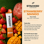 A promotional product graphic for Stacked Strawberry Mango flavor powder. The left side shows a single Stacked stick pack surrounded by fresh strawberries, mango pieces, and a pink drink on a green textured surface.