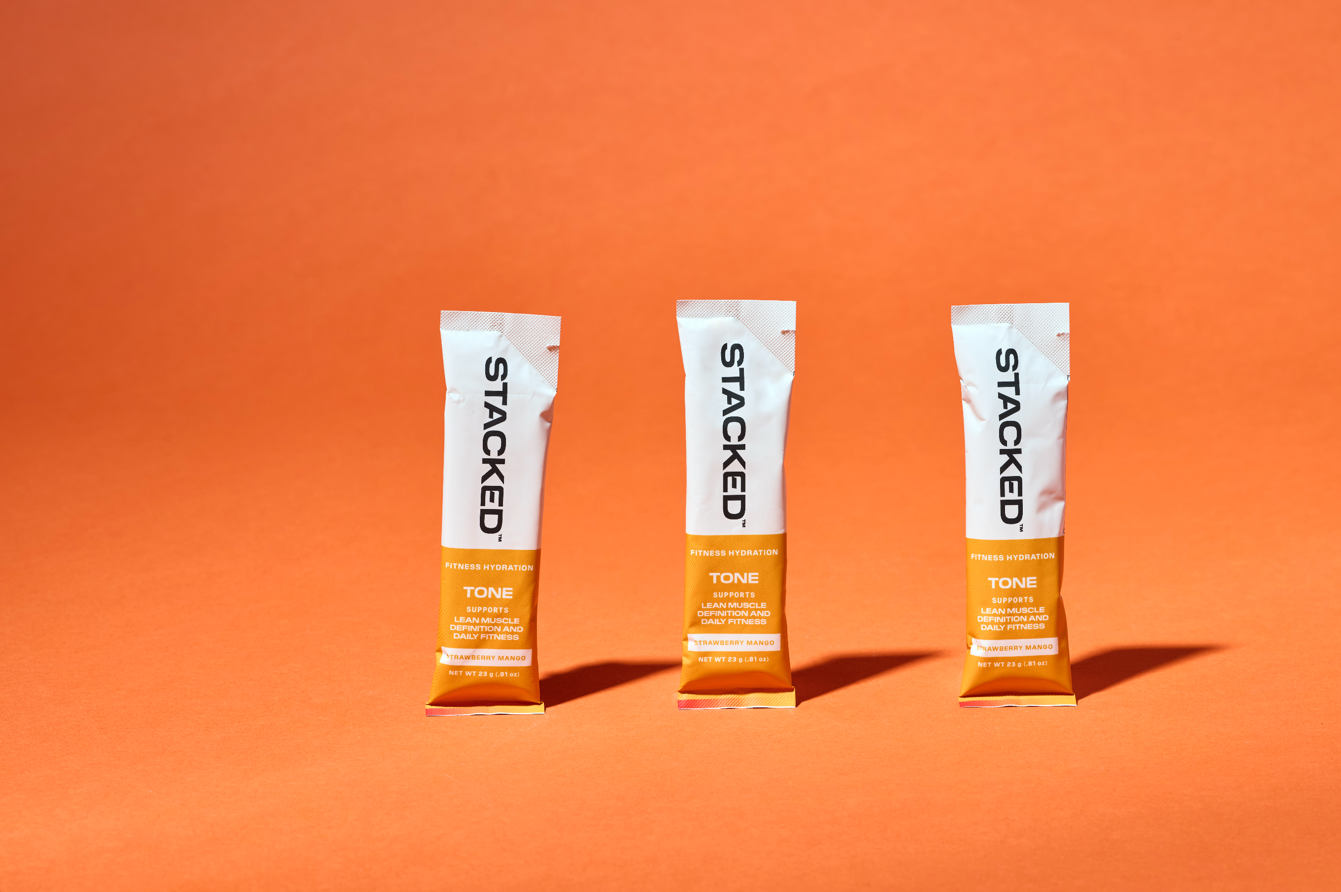 Three 'Stacked' hydration powder packets on an orange background