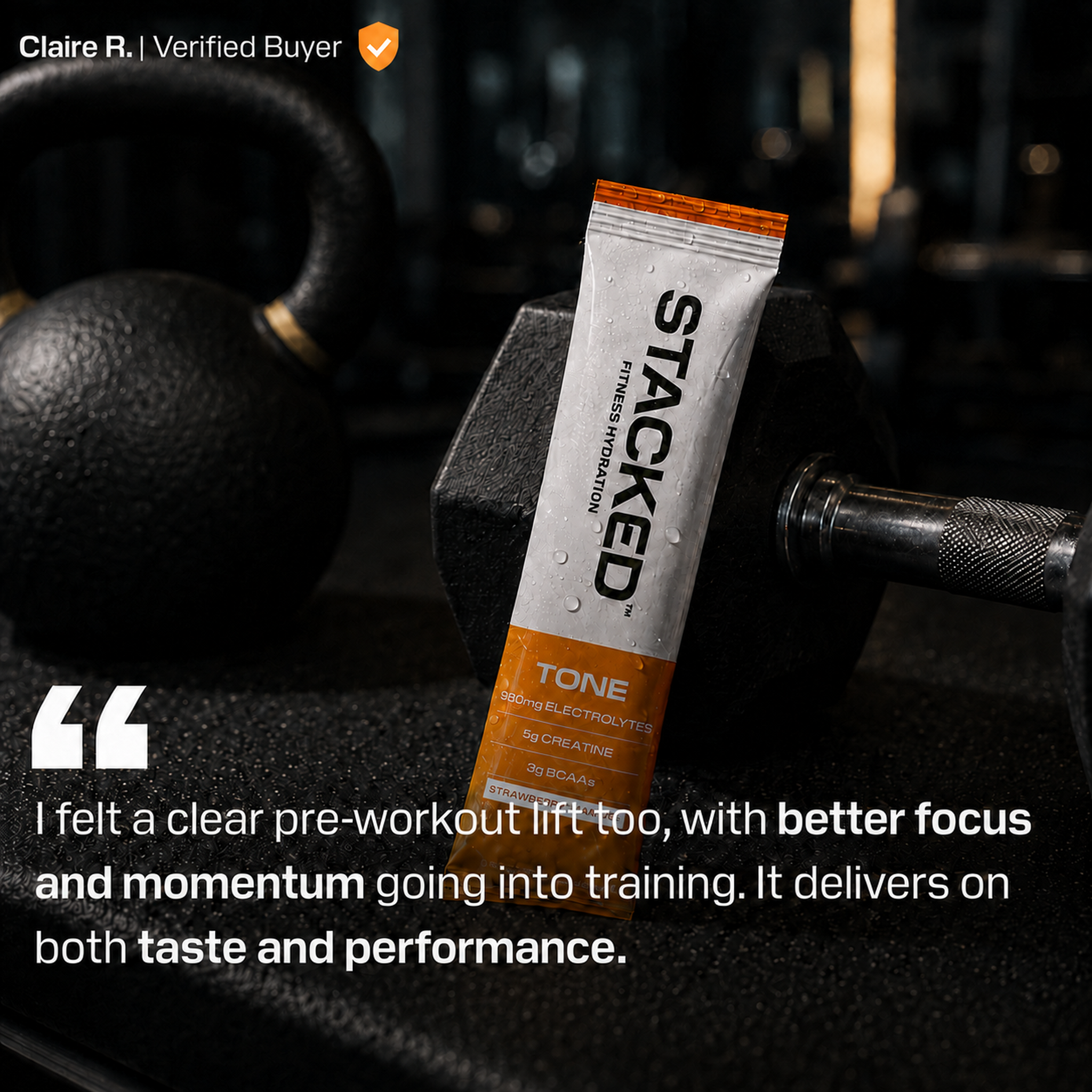 A single STACED pre-workout supplement tube standing upright on a gym floor between two black dumbbells, with a blurred gym background and a customer testimonial quote overlaid at the bottom.