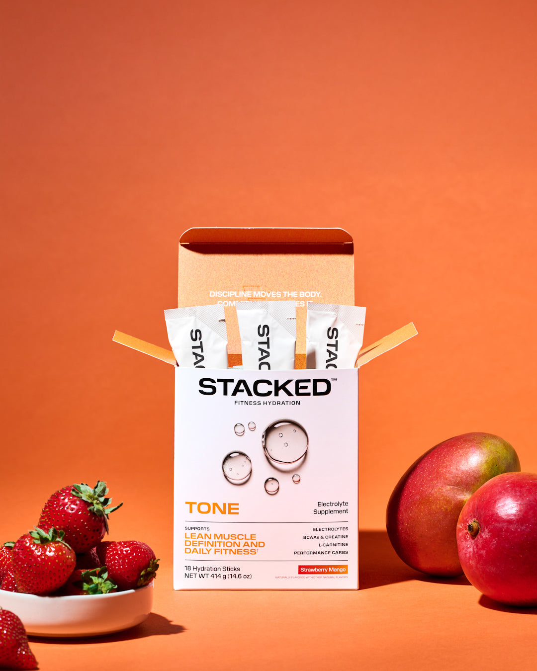 Stacked supplement packaging with strawberries and mangos on an orange background