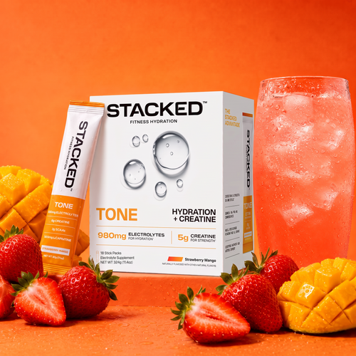 Stacked TONE Creatine + Hydration, Strawberry Mango 18-pack box with a stick pack, a glass of pink drink, fresh strawberries and mango on an orange background